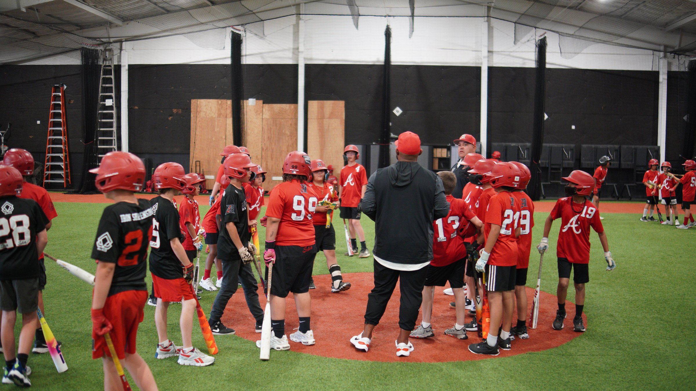 An Admirals youth baseball team in red jerseys gathers around their coach on the infield at The ACE in Vacaville