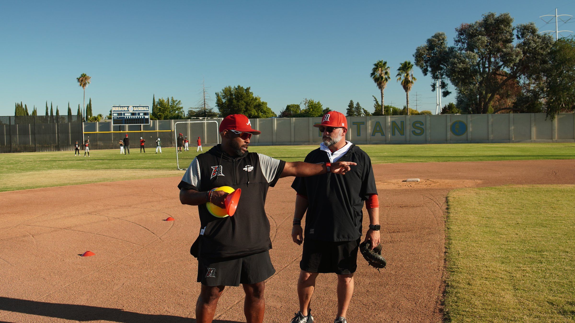 Two Admirals coaches talk through a drill on the infield at an outdoor practice in Sacramento