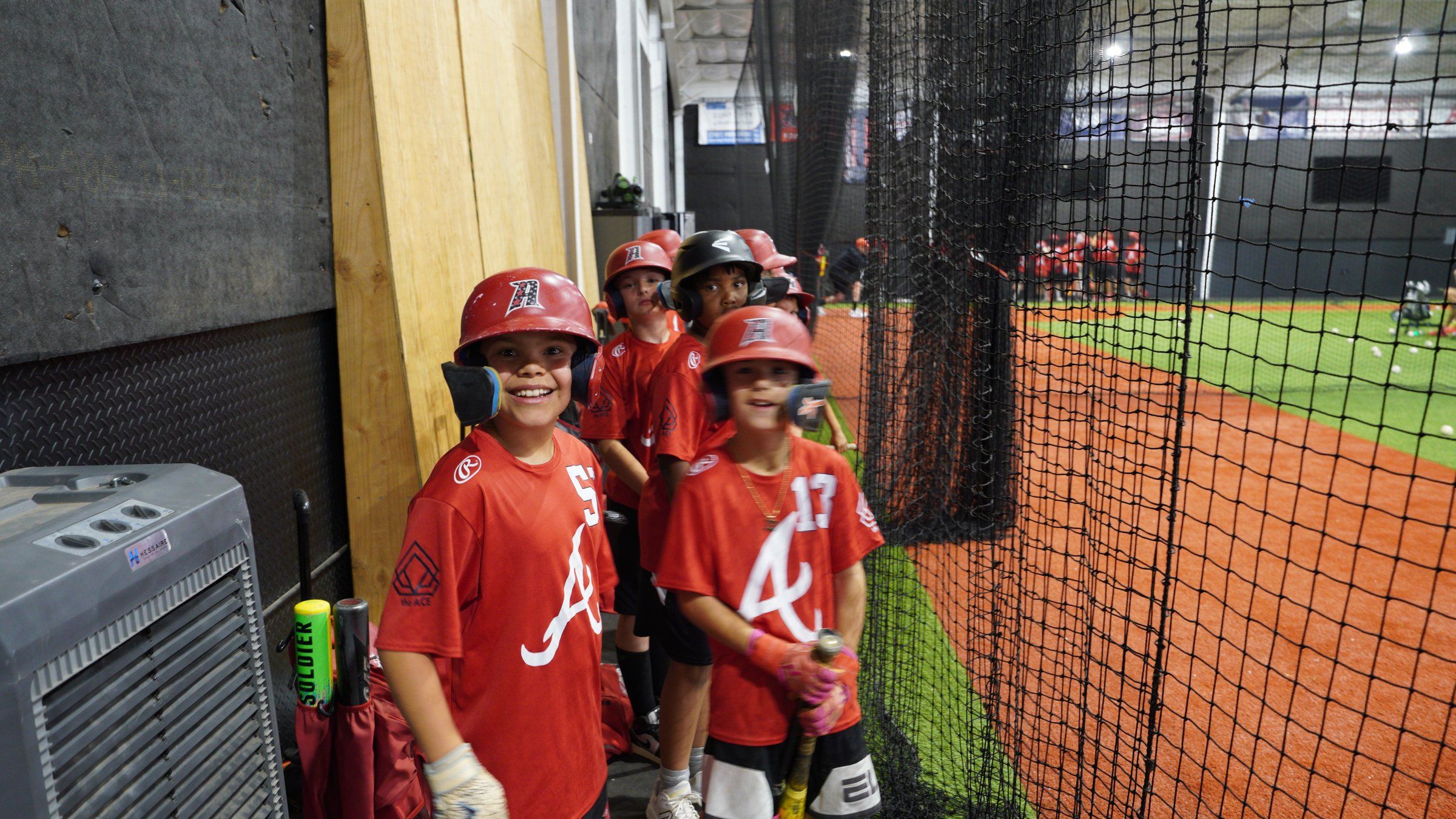 Young Admirals players grin in their red jerseys while waiting to hit at The ACE in Vacaville