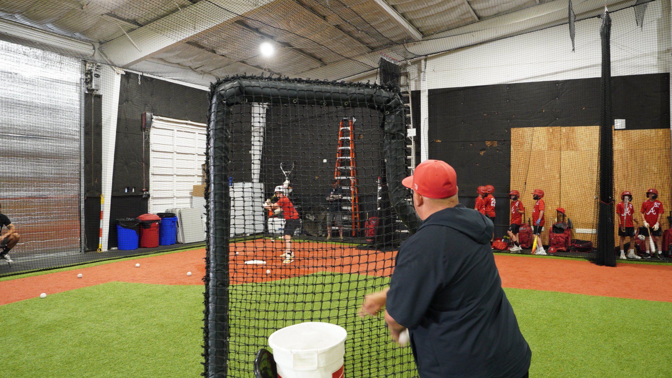 An Admirals coach feeds batting practice from behind an L-screen while a hitter waits at The ACE in Vacaville