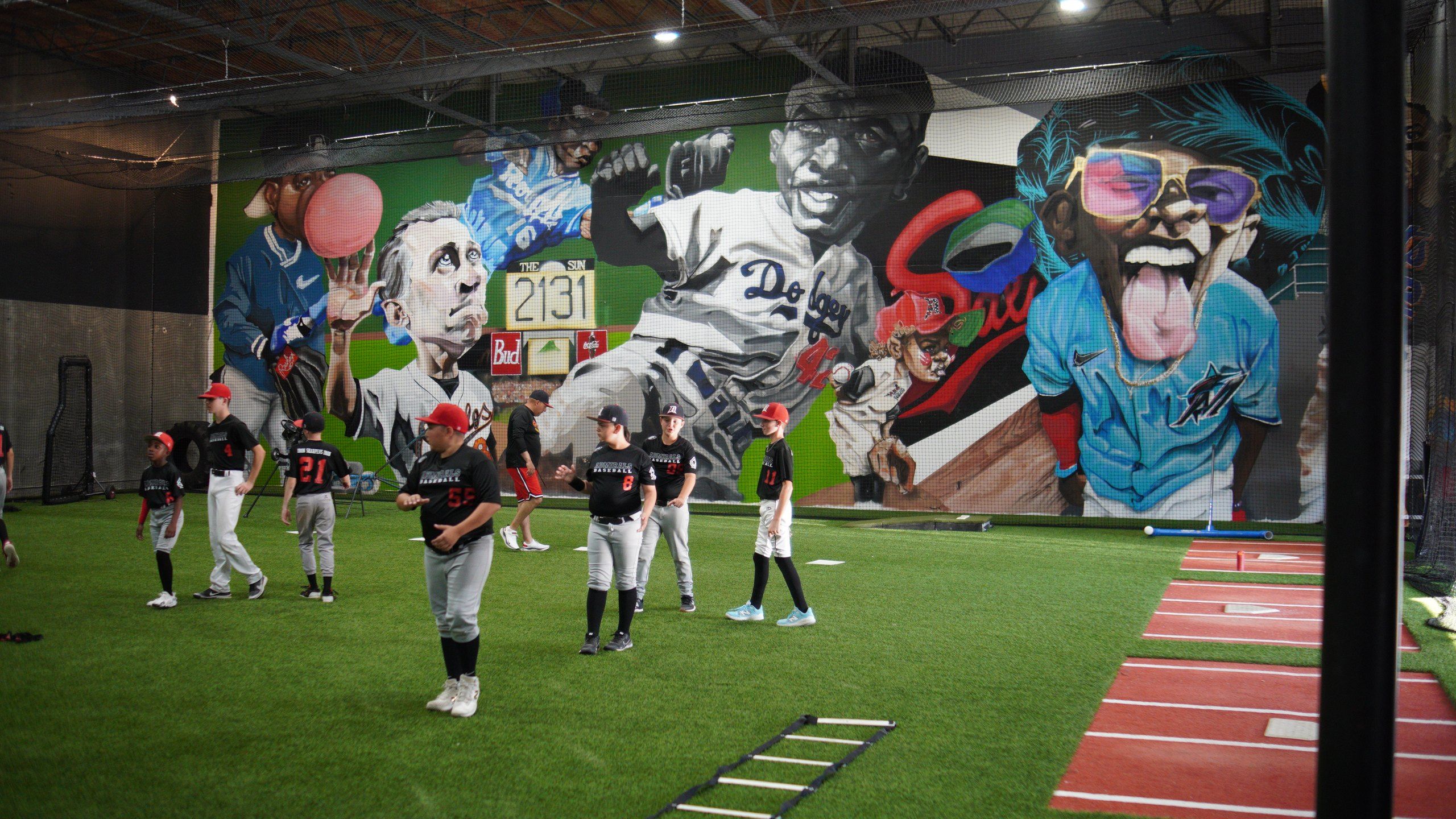Admirals players run agility drills on indoor turf in front of a large baseball mural at the Sacramento facility